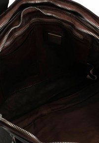 Interno di una borsa in pelle marrone con molteplici tasche con zip, superfici testurizzate e un ampio compartimento principale. L'imbottitura è liscia e scura.
