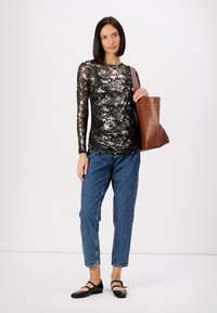 Svart langermet topp med paljettmønster, blå høyhårede jeans og svarte leiligheter. Brun toteveske med en enkelt skulderstropp.
