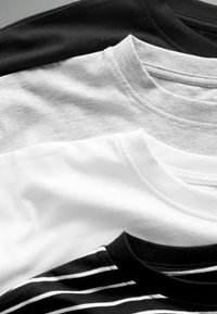 Quattro t-shirt impilate: nera, grigia, bianca e con un design a righe nere. Materiale in cotone con scollature rotonde e semplici dettagli di cucitura.
