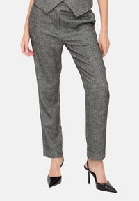 Graue, schmal zulaufende Hosen im Fischgrätenmuster, hoch tailliert, mit strukturierter Stoffqualität, schlanker Passform, kombiniert mit schwarzen spitzen High Heels.
