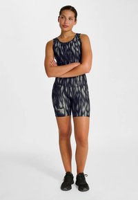 Svart atletisk bodysuit med vågmönster, figurnära design, ärmlös och matchande shorts. Inkluderar en liten logotypaccent.