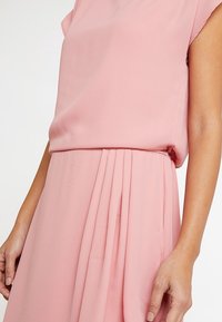 Ljusrosa chiffongklänning med en avslappnad passform, korta ärmar och plisserade detaljer vid midjan, samt en mjuk och lätt textur.