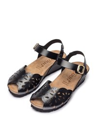 Black leather sandals with cut-out floral designs, open toe, cork insole, and ankle strap with decorative buckle. Flat rubber sole.