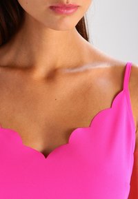 Haut sans manches fuchsia avec un décolleté à bords festonnés. Confectionné en tissu lisse, il présente des bretelles fines et une silhouette ajustée.