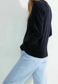 Svart långärmad topp i mjukt material, figurnära stil. Kombinerad med ljusblå byxor, sidoficka synlig, slät textur på båda.