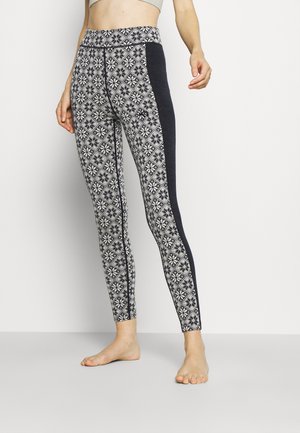 Leggings with a patterned fabric featuring a diamond and snowflake design in white and navy, with a solid navy side panel and high waistband.