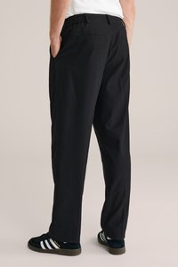 Svarta byxor med avslappnad passform, elastisk midja, sidofickor och en mjuk yta. Matchas med gröna och svarta sneakers.