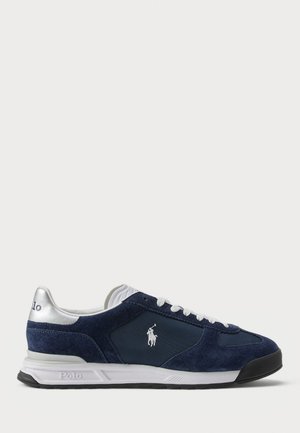 Navy blue suede sneakers with white lace-up closure, silver accents on the heel, and a logo on the side. Rubber outsole for traction.