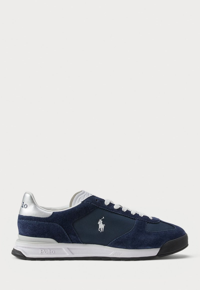Baskets en velours bleu marine avec fermeture à lacets blanche, accents argentés au talon et logo sur le côté. Semelle en caoutchouc pour une meilleure traction.