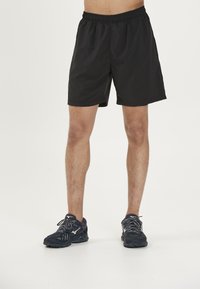 Zwarte sportshorts van lichtgewicht materiaal, met een elastische tailleband en een comfortabele pasvorm. Draagt met donkere hardloopschoenen.