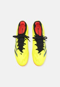 Botas de fútbol amarillas luminosas con cordones y acentos negros. Presentan una parte superior sintética texturizada y un interior acolchado rojo.