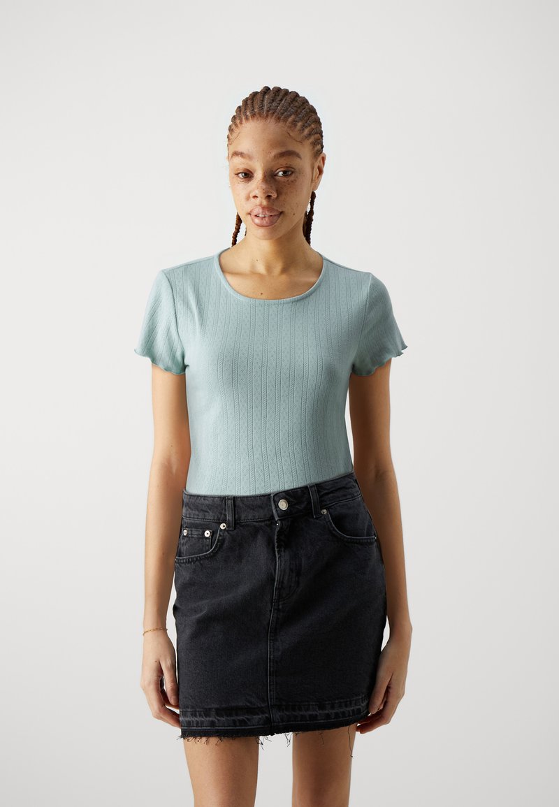 Haut bleu clair à manches courtes avec une texture côtelée et un col rond, associé à une jupe en denim noir avec un ourlet effiloché et des poches avant.