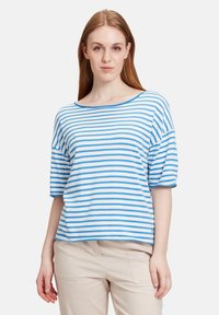 Niebiesko-białe paskowane, krótkie rękawy, bluzka z dekoltem w łódkę, luźny fason i miękka faktura, w połączeniu z jasnymi spodniami.