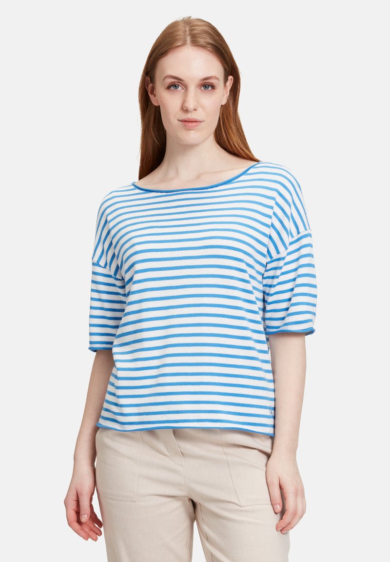 Niebiesko-białe paskowane, krótkie rękawy, bluzka z dekoltem w łódkę, luźny fason i miękka faktura, w połączeniu z jasnymi spodniami.