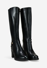 Botas de cuero negras hasta la rodilla con tacones cuadrados y cierre lateral, que cuentan con correas decorativas y una hebilla en la zona del tobillo.