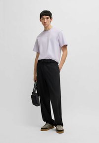 Tricou scurt lavandă, asortat cu pantaloni negri cu talie înaltă. Modelul ține o geantă neagră și poartă adidași gri și maro. Design simplu.