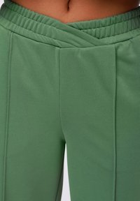 Pantaloni sportivi verdi realizzati in tessuto liscio, con una cintura larga e testurizzata e due pieghe frontali per un tocco di dettaglio in più.