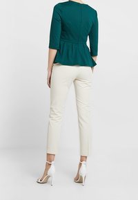 Teal peplum top met driekwart mouwen, gecombineerd met crèmekleurige slim-fit broeken, aangevuld met witte hoge hakken.