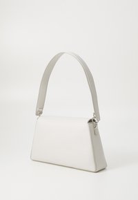 Petit sac à main en cuir blanc avec une large bandoulière et une quincaillerie argentée sur un fond blanc uni.