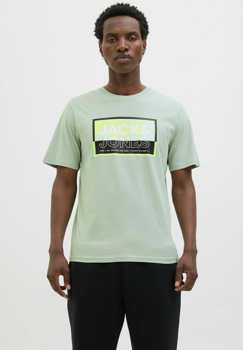 Lichtgroen katoenen T-shirt met een opvallend zwart en neon grafisch logo "JACK & JONES" in rechthoekig ontwerp. Korte mouwen, ronde hals.