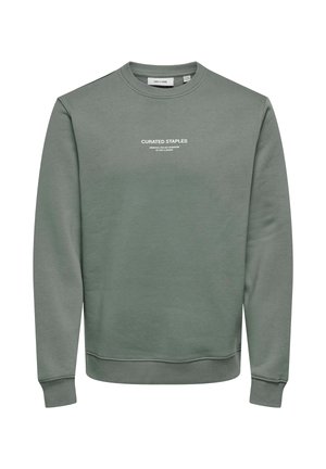 Zeleni pulover iz mehkega materiala, s krožnim izrezom, dolgimi rokavi in belim napisom spredaj. Gladko teksturo, minimalistična zasnova.