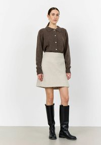 Brun knapp-up tröja med krage, tillsammans med en ljusgrå ull A-linjekjol. Svarta knähöga läderstövlar fulländar outfitten.