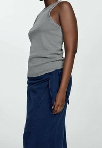 Grijze geribde tanktop met een hoge halslijn, gecombineerd met een donkerblauwe wikkelrok, voorzien van een zijknoop en een gladde stoftextuur.