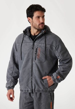 Gray hooded jacket with a zip closure, elastic cuffs, and a front pocket. Features logo detail in orange and a textured fabric finish.