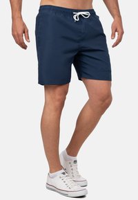 Marine zwemshorts met een elastische tailleband en witte trekkoord. Heeft een soepele textuur en subtiele logo-detail aan de zijkant. Draagt u met witte sneakers.