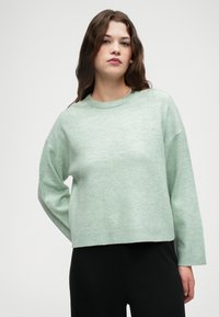 Pulover v mint zeleni barvi, izdelan iz mehkega pletenega materiala. Ima okroglo ovratnico, spuščene ramena in rebrast rob. Kratka dolžina.
