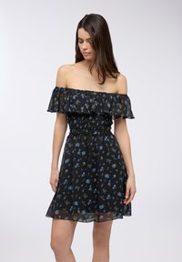 Abito nero a spalle scoperte con motivi floreali in blu e verde. Presenta un corpetto smock e una gonna fluida con dettagli trasparenti sull'orlo.