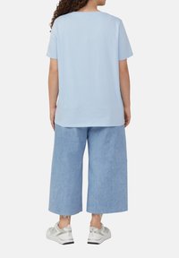 Lichtblauwe katoenen T-shirt met korte mouwen, ontspannen pasvorm, gecombineerd met lichte denim culottes en witte sneakers. Casual en comfortabele stijl.