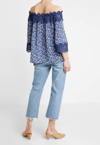 Off-the-shoulder blå blommig topp med spetsdetaljer, matchad med ljusblå fransiga jeans och beige klackskor med blockklack.