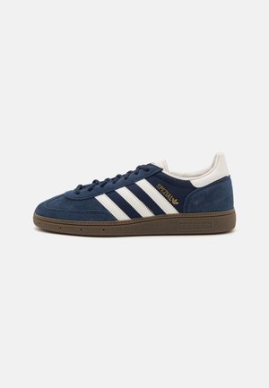 Niskie granatowe zamszowe trampki Adidas z białymi paskami, złotym napisem "SPEZIAL", białą pętelką na pięcie i brązową gumową podeszwą.