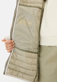 Gevoerde, lichtgrijze jasinterieur met een gladde textuur, voorzien van een waterafstotende, winddichte laag en dons-vrije iconen in het geel.