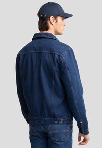 Temno modra denim jakna z gumbastim zapiranjem, klasičnim ovratnikom in dolgimi rokavi. Ima dva gumba kot okras na pasu in ukrivljene šive.