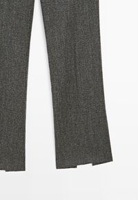 Gambe di pantaloni in tessuto a costine grigio scuro con una leggera svasatura e piccole fessure all'orlo su uno sfondo bianco.