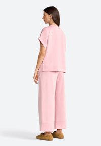 Pink oversized sweatshirt with short sleeves, paired with wide-leg pants. Soft material with a smooth texture. Accented by visible seams and cuffs.