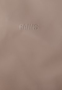 Rózsaszín vízálló anyag, sima tapintással, az "RAINS" felirattal domború mintázattal, minimalista dizájnnal.