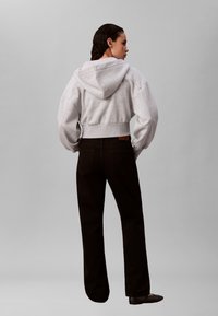 Grijze cropped hoodie met capuchon, gedragen met zwarte wijde broekspijpen. De hoodie heeft geribbelde boorden en de broek heeft achterzakken.