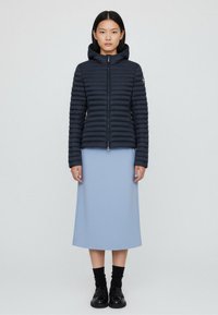 Navy puffer jacket with horizontal quilted design, front zip, and hood. Worn over a light blue midi dress, paired with black socks and shoes.
