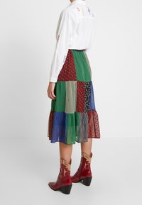 Laatikkomainen hame, jossa kerroksittainen muotoilu ja erilaisia värejä ja kuvioita, yhdistetty punaisiin cowboy-saappaisiin. Valkoinen paita, jossa kirjailu.