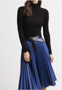 Svart riplädd turtlenecktröja som är matchad med en blå plisserad kjol. Kjolen har ett svart bälte som framhäver midjan.