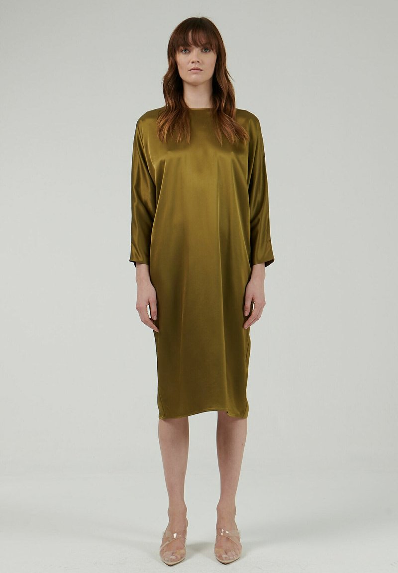 Vestido de satén verde oliva con un corte holgado, dobladillo hasta la rodilla y mangas largas, que presenta un escote redondo y una textura suave y brillante.