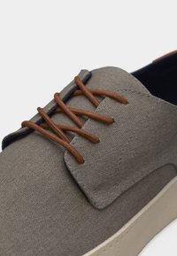 Chaussure décontractée en tissu gris avec des lacets marron et une semelle blanche, vue en gros plan de côté et de dessus.