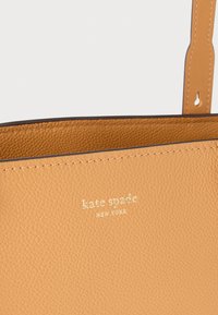 Τσάντα tote από ταμπά δέρμα με υφή στην επιφάνεια, με χρυσό ανάγλυφο λογότυπο "kate spade NEW YORK" και λείες άκρες. Διαθέτει ρυθμιζόμενες λαβές.