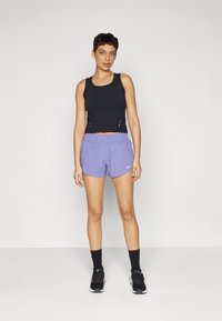 Black cropped tank top with side cutouts, paired with light purple athletic shorts featuring an elastic waistband and white logo. Black sneakers.