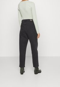 Svarta högmidjade jeans i denim med bakfickor, i kombination med en ljusgrön långärmad tröja och gröna ankelstövlar med krokodilskinnsmönster.