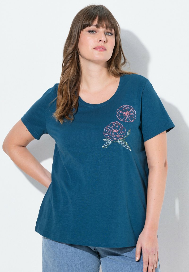 Turkoosi t-paita lyhyillä hihoilla, pyöreällä kaula-aukolla, jossa on vaaleanpunaisia ja vihreitä kukka-embroideryitä vasemmalla puolella. Pehmeä, kevyt kangas.