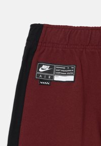 Bordo un melnā sporta šorti ar izšūtu jostu un zīmola etiķeti ar "Nike Air" tekstu un dizaina detaļām.